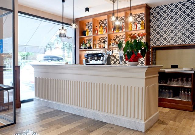 Bar con bancone bianco, scaffali in legno con bottiglie e parete decorata.