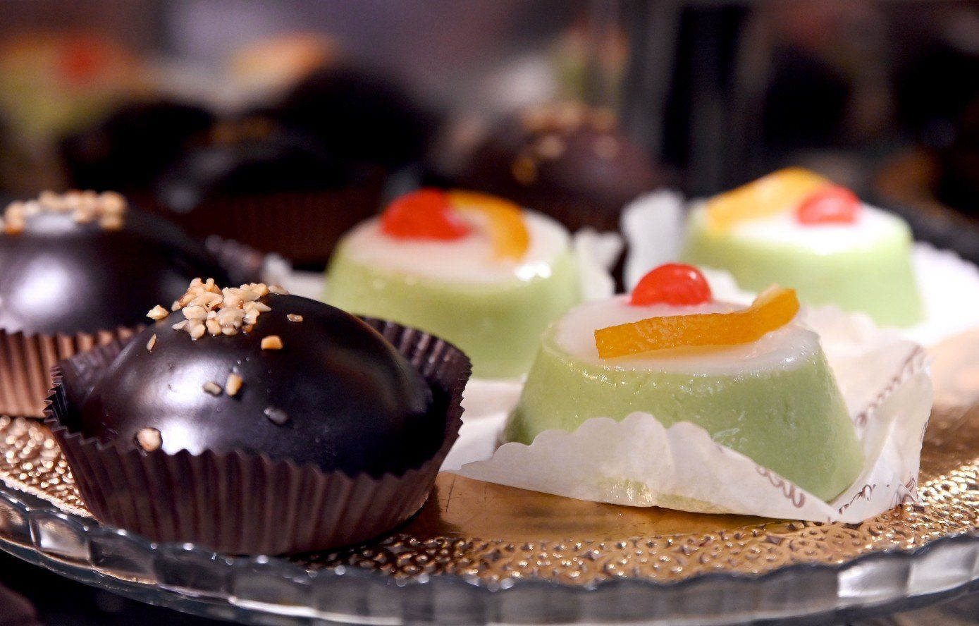 Primo piano di pasticcini: cupole di cioccolato fondente e torte color pastello con frutta su un vassoio decorativo.