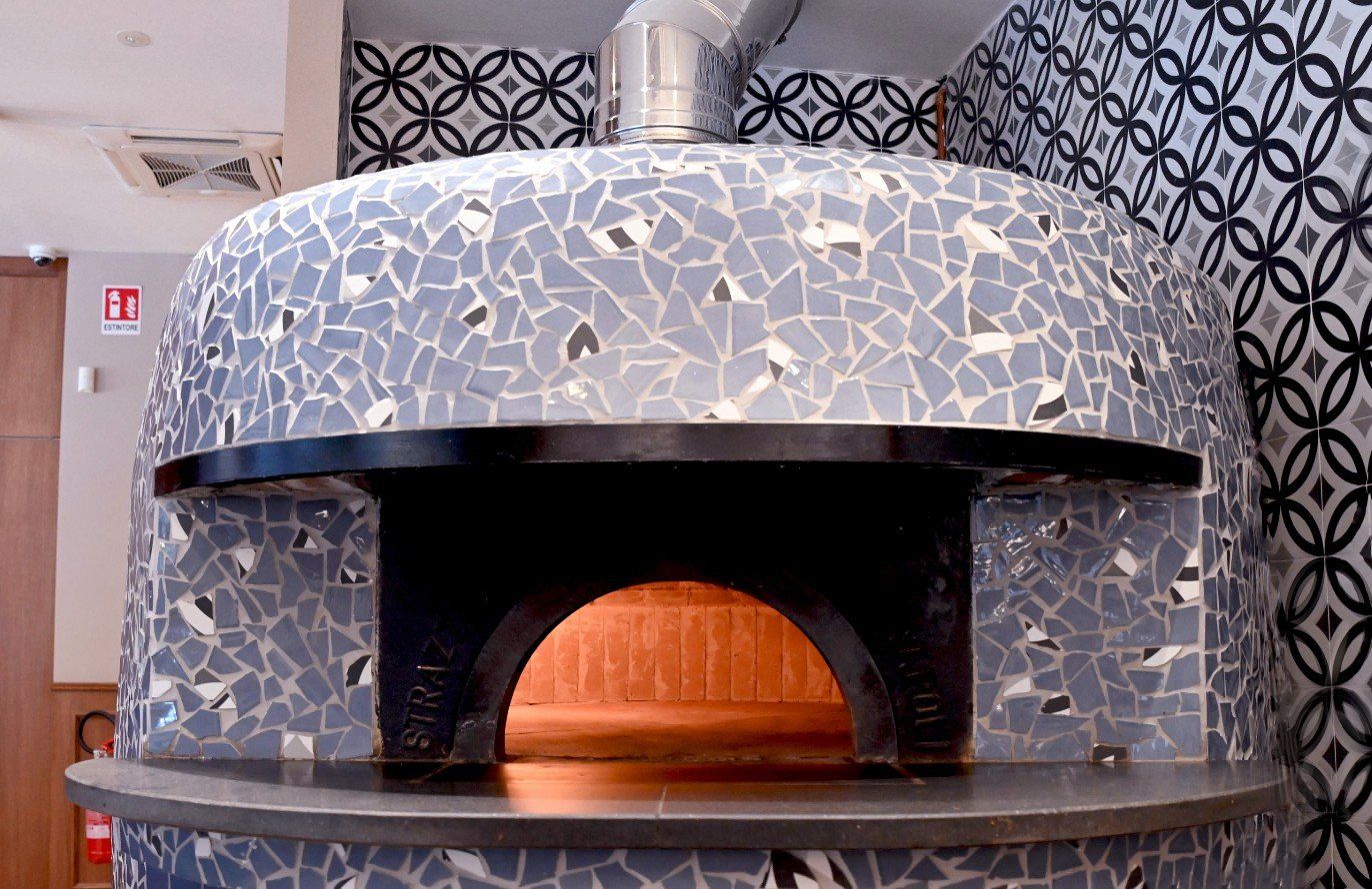 Forno in pietra con rivestimento esterno in piastrelle a mosaico, canna fumaria e facciata anteriore aperta.