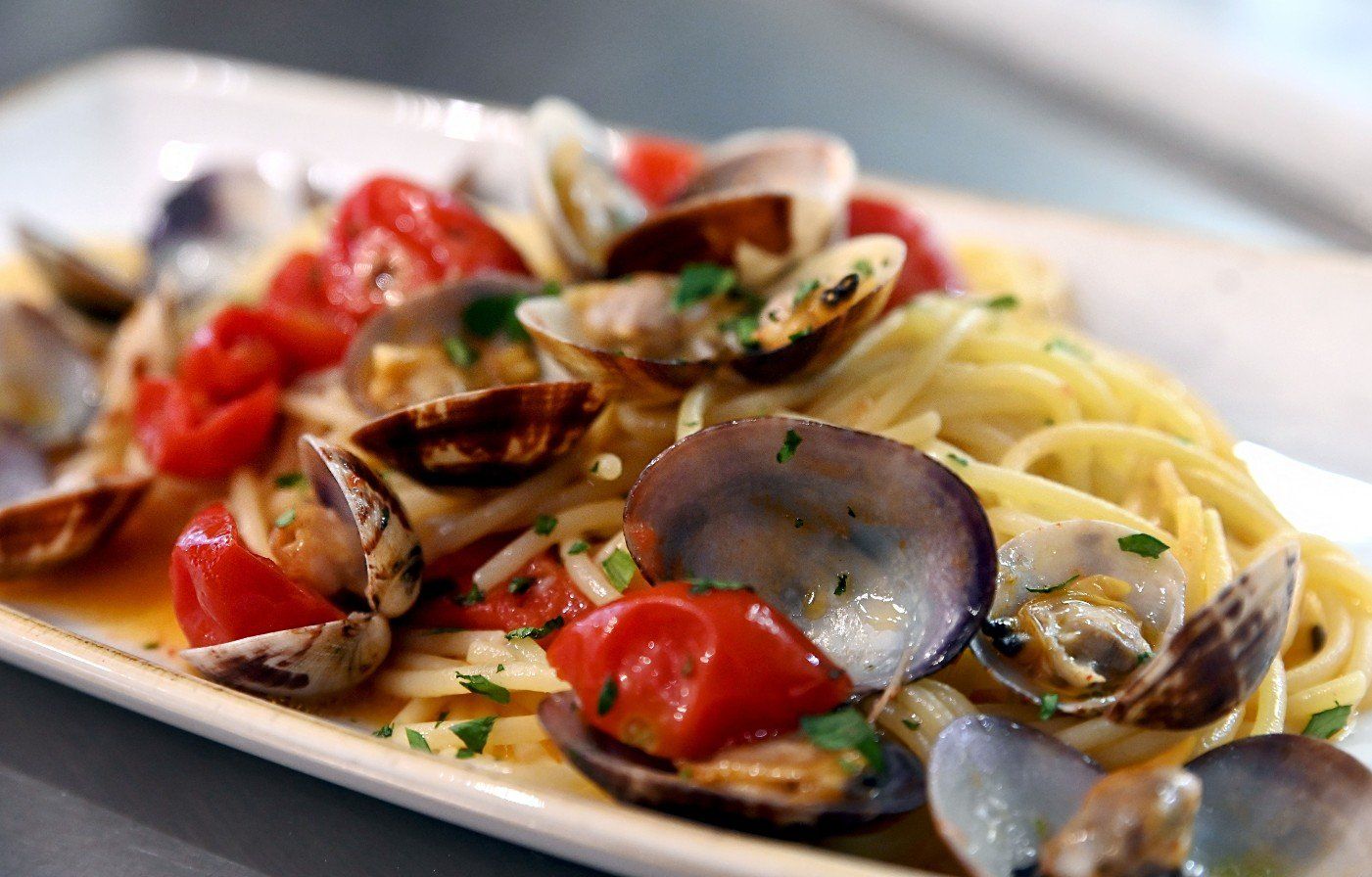 Spaghetti con vongole e pomodorini su un piatto bianco rettangolare.