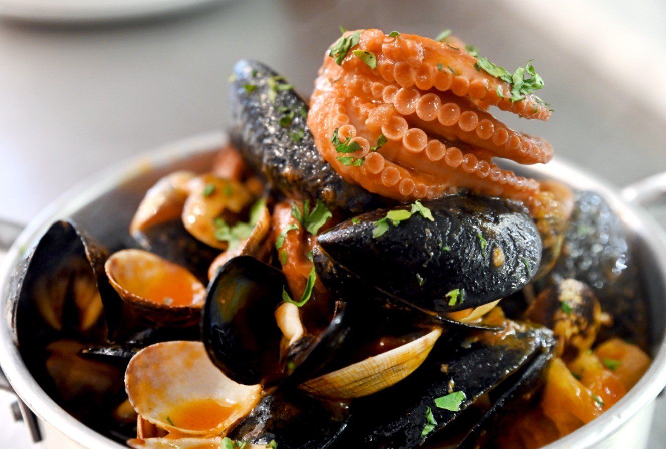 Stufato di pesce: polpo, cozze e vongole in una ciotola di metallo, guarnito con prezzemolo.