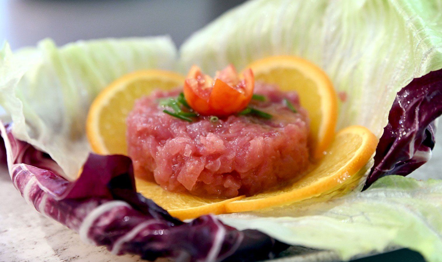 Un piccolo cumulo di cibo rosa, guarnito con fette d'arancia e lattuga, sormontato da un pomodoro.