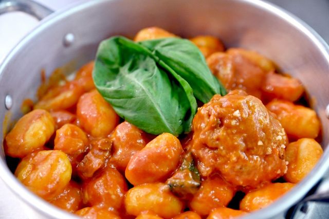 Gnocchi al sugo di pomodoro, conditi con basilico, in una pentola d'argento.