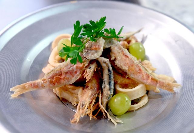 Piatto di frutti di mare fritti con guarnizione di uva e prezzemolo su un piatto di metallo.
