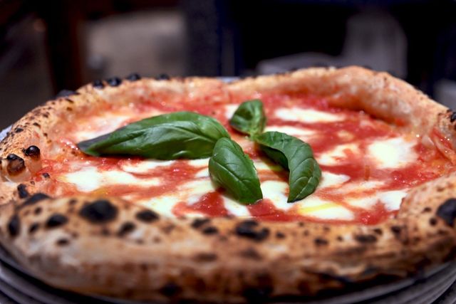 Primo piano di una pizza Margherita con foglie di basilico. La crosta è bruciacchiata. Salsa rossa e formaggio bianco.