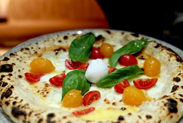Pizza condita con pomodori gialli e rossi, mozzarella e basilico su una crosta maculata.