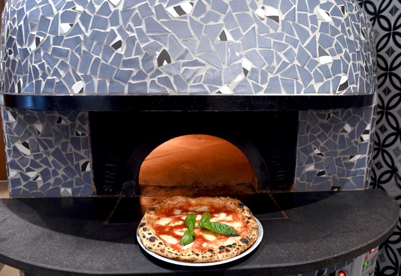 Pizza appena sfornata dal forno a legna. La pizza è condita con salsa di pomodoro e basilico.