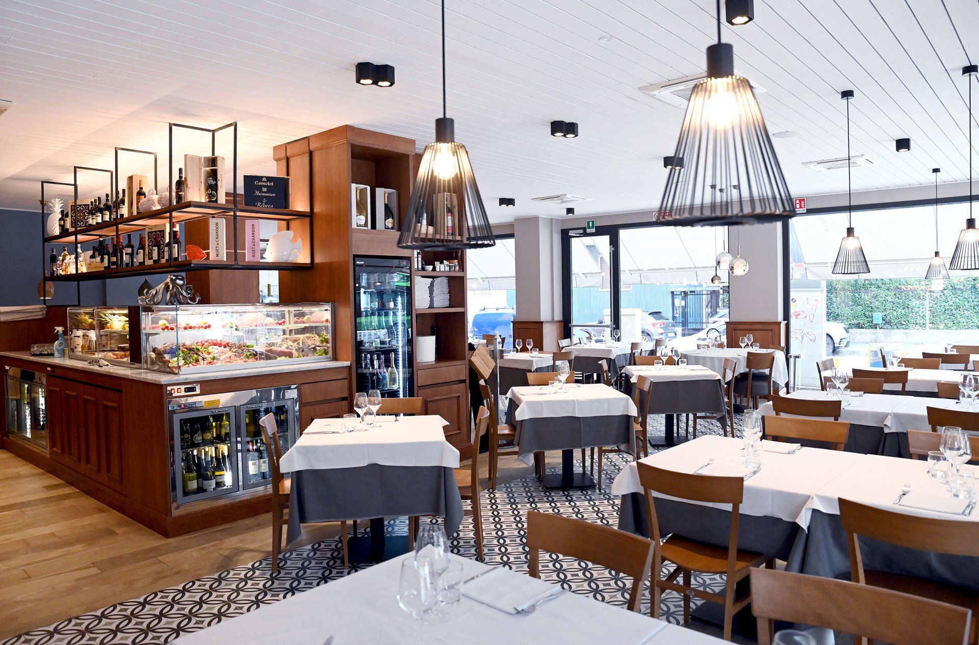 Interno del ristorante con tavoli apparecchiati per mangiare e un'area bar con esposizione di vini e cibo.