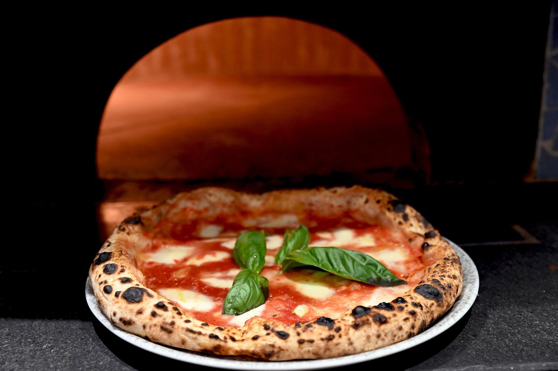 Pizza con foglie di basilico, davanti al forno a legna.