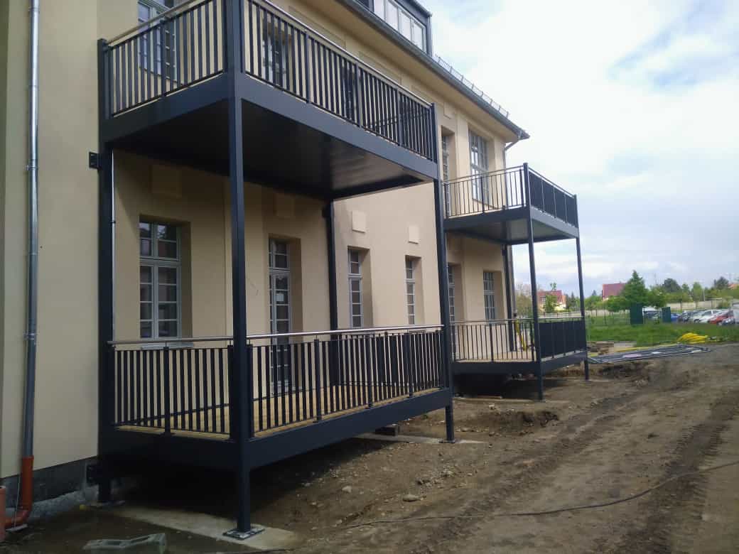 Zweistöckiges beigefarbenes Haus mit dunklen Balkonen und Veranden an einem unbefestigten Weg, das sich im Bau befindet