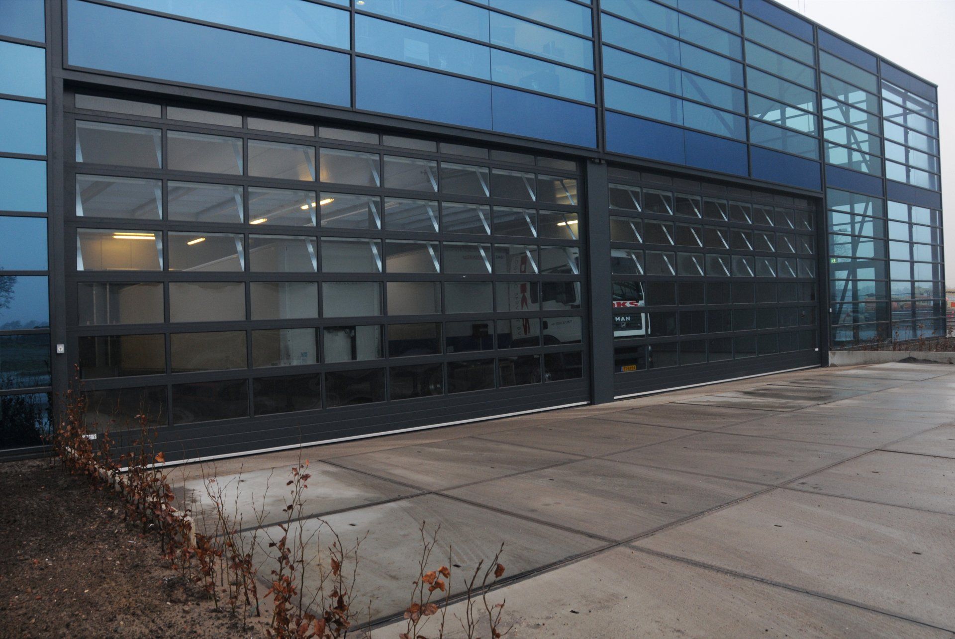 Modernes Industriegebäude mit Glasfassade, großen Garagentoren und betoniertem Vorplatz