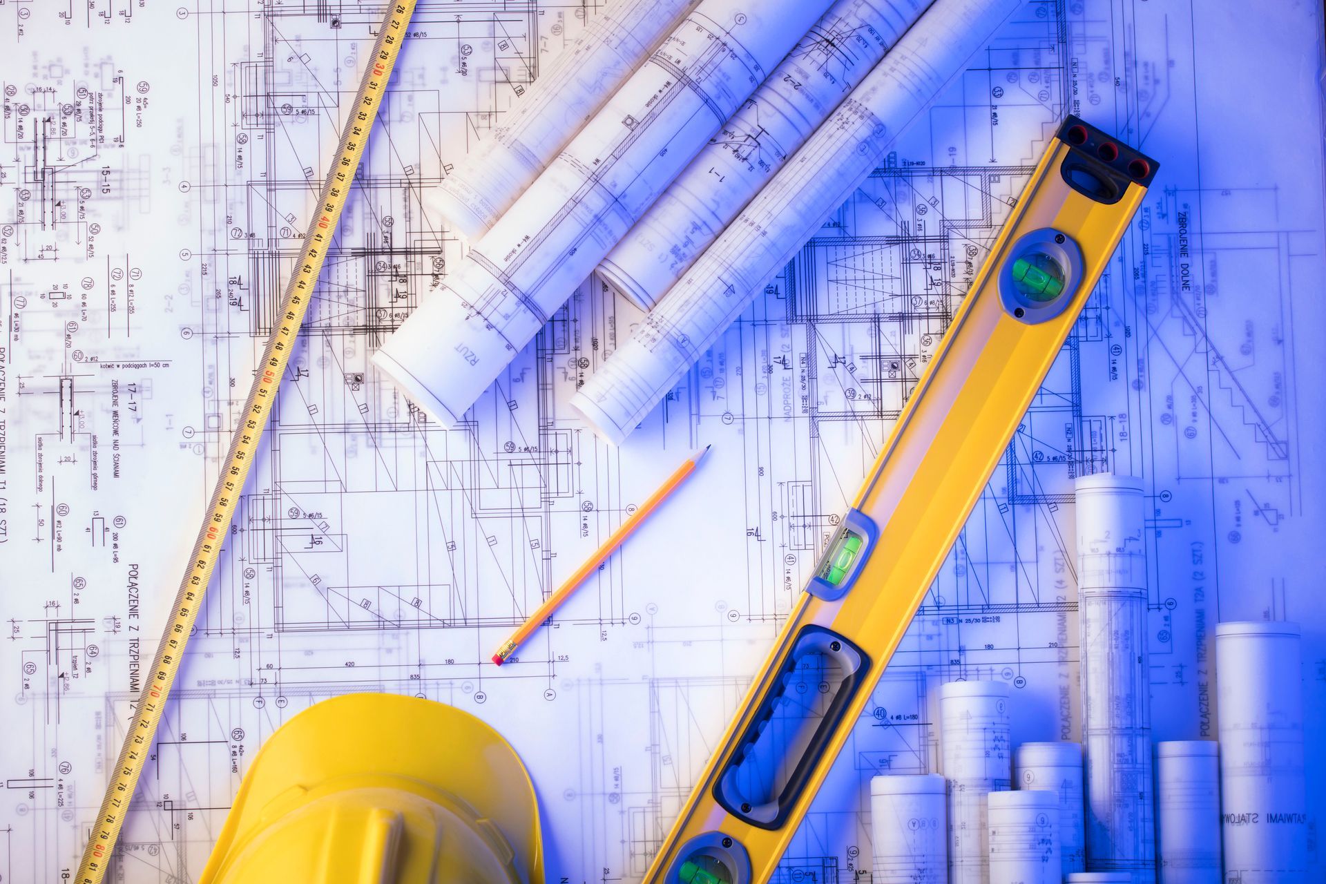 A hard hat , level , tape measure , and pencil are on top of a blueprint.