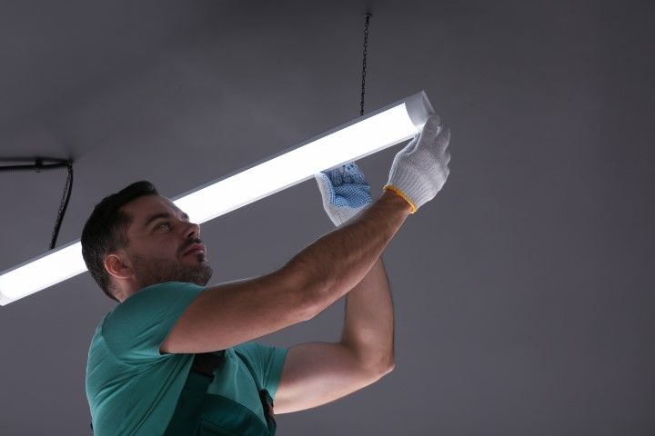 Man installing a fluorescent light fixture on a ceiling with a screwdriver and gloves