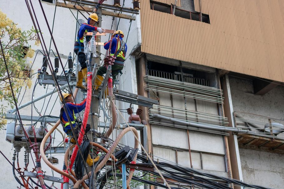 Utility workers on a utility pole with tangled cables beside a building