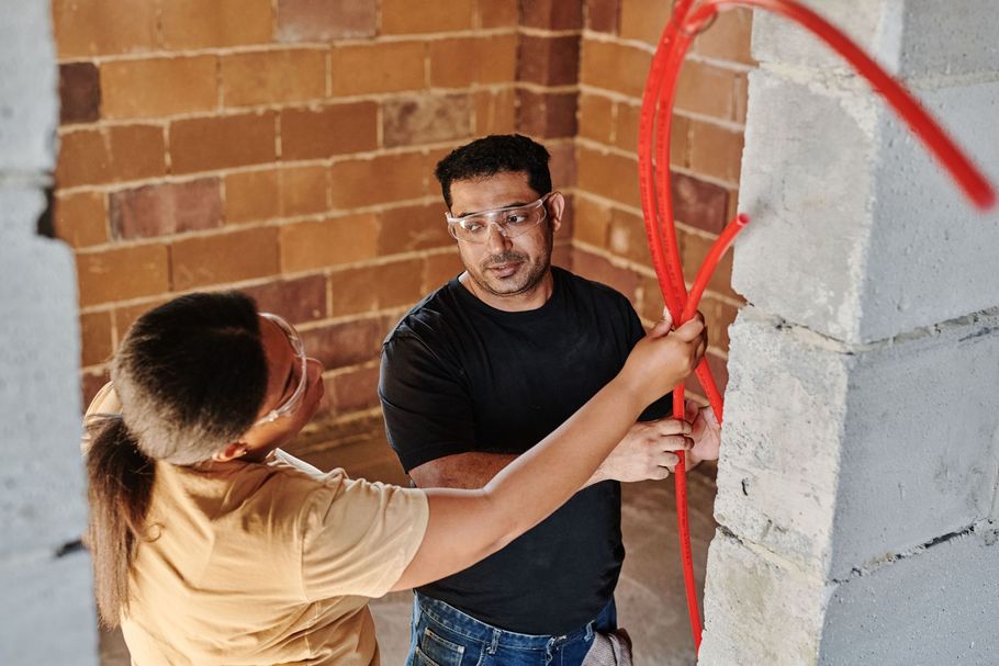 Two people inspecting a wall with red spray markings in an unfinished brick interior