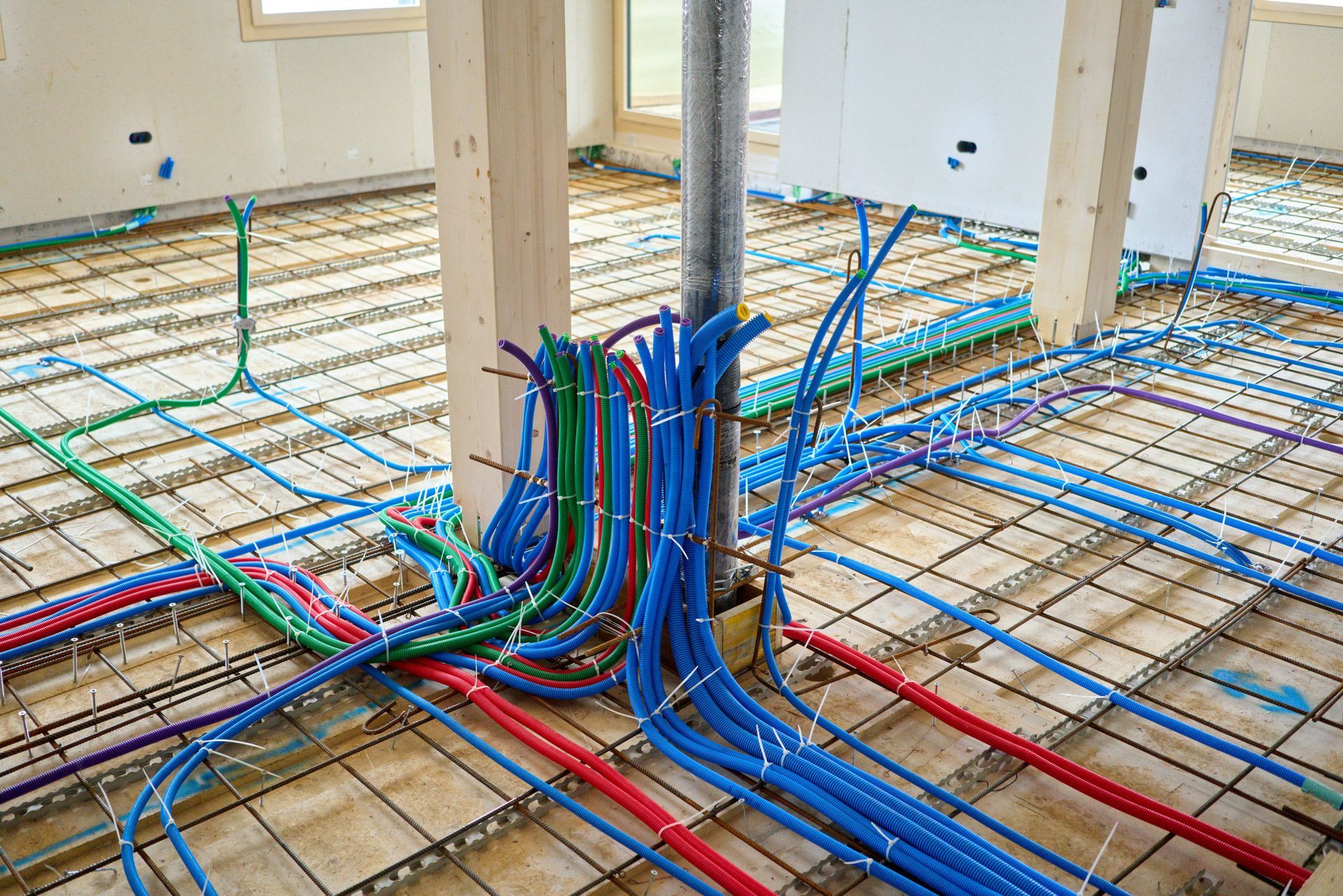 Colorful electrical wiring laid across a house floor under construction, with pipes and conduits rising from the center.