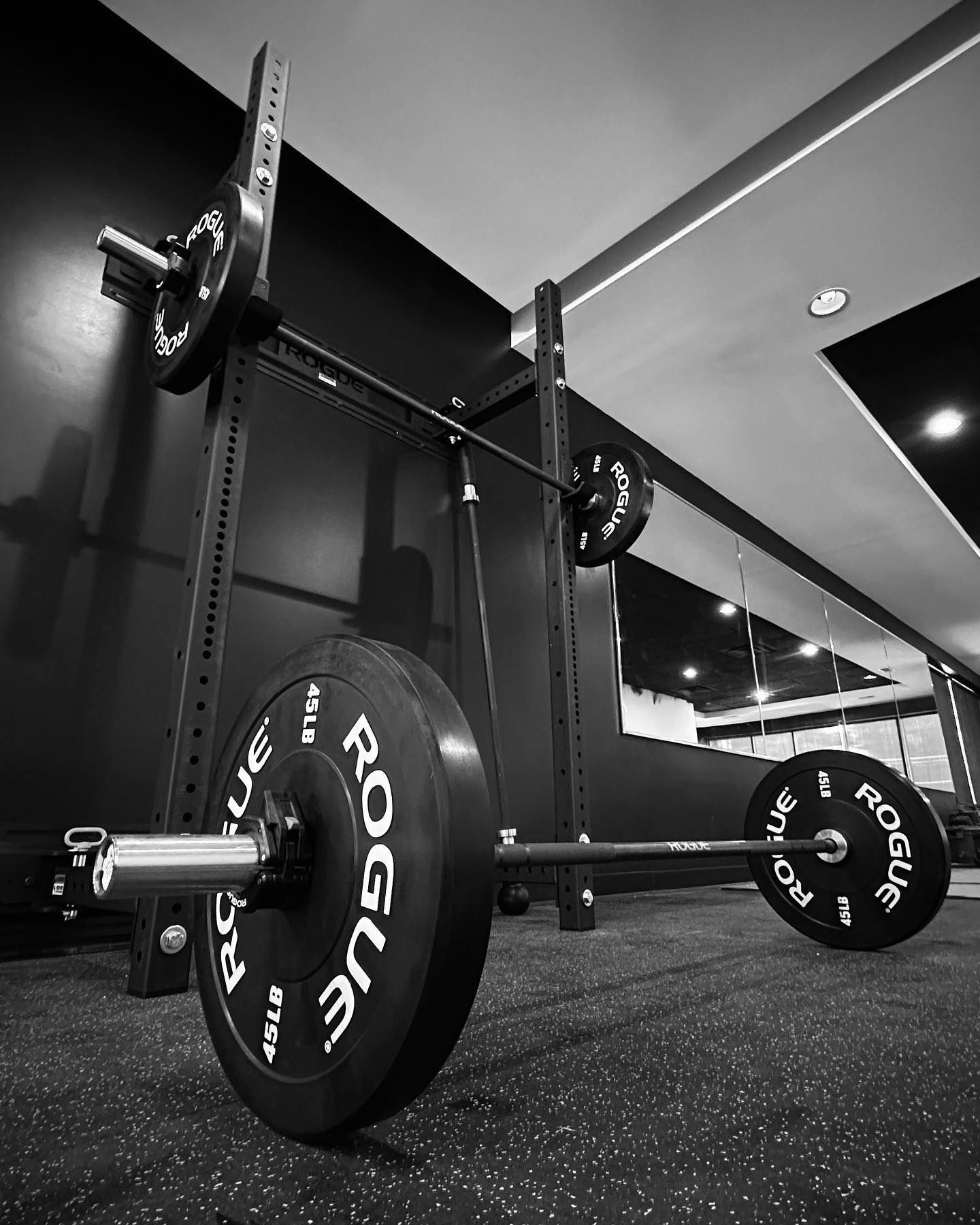 Barbell loaded with weight plates in a gym setting. The bar rests in a squat rack.