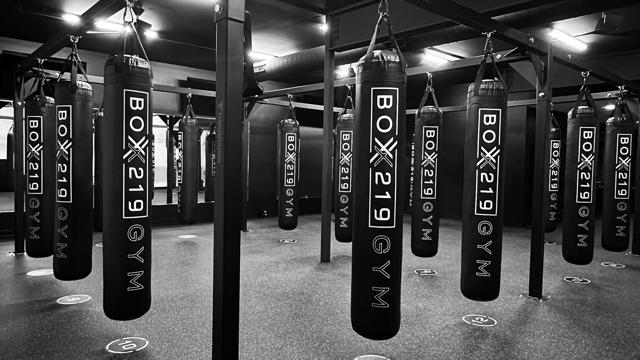 Boxing gym with several black heavy bags hanging from the ceiling, marked 