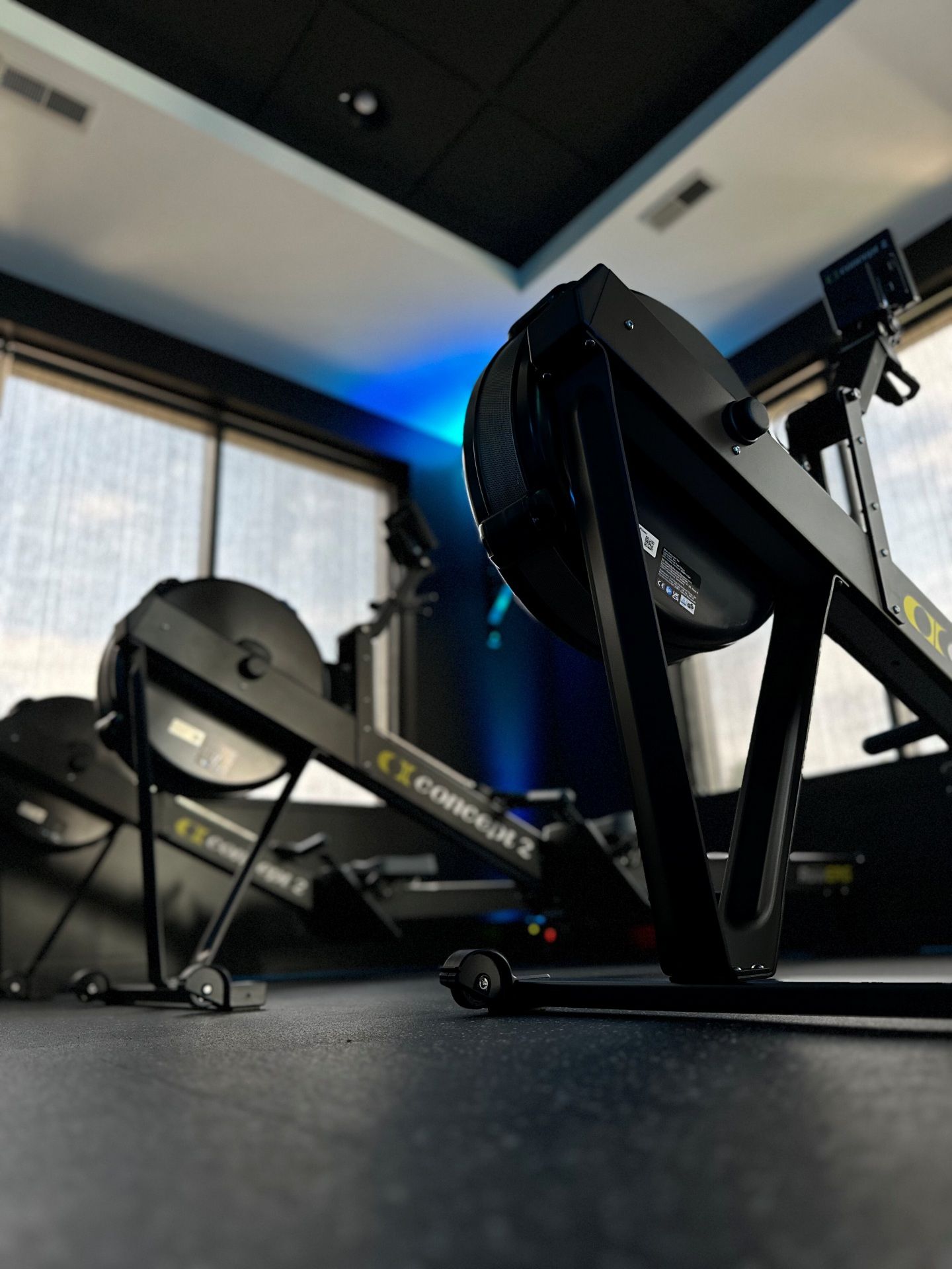 Rowing machines in a gym with dark walls and windows, illuminated by blue light.