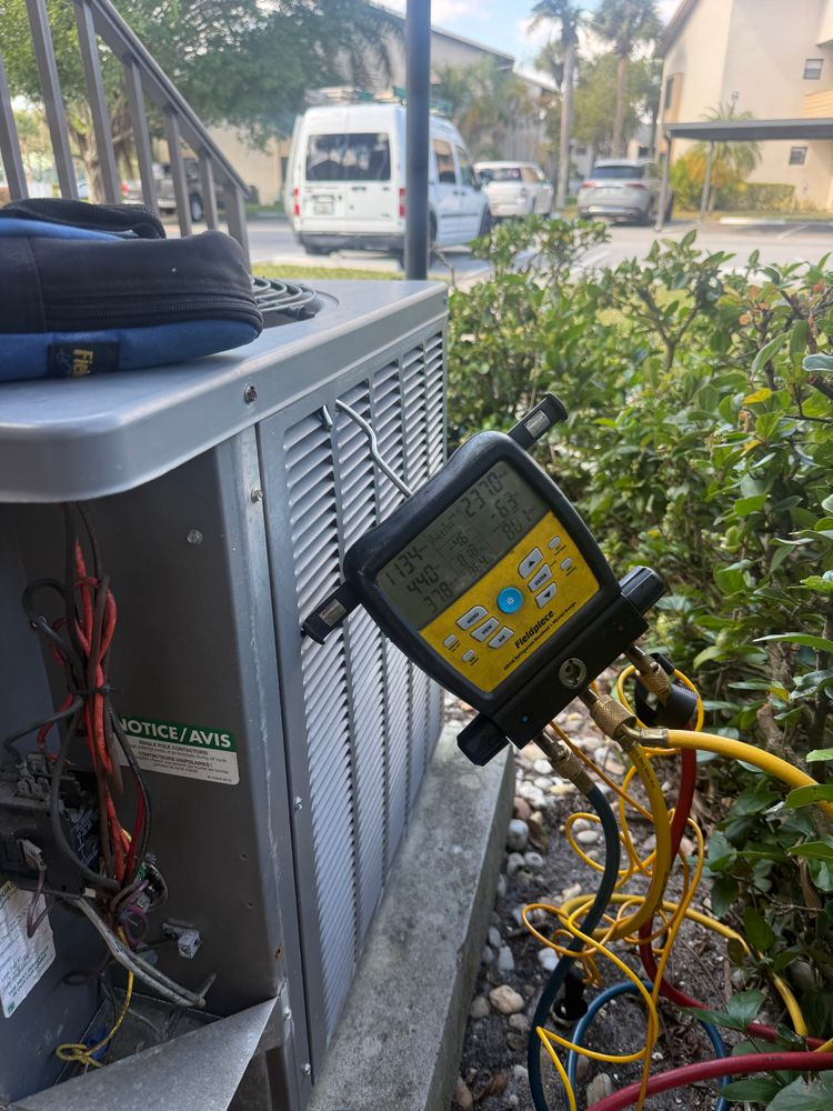 Yellow diagnostic meter attached to an outdoor HVAC unit with exposed wiring and hoses