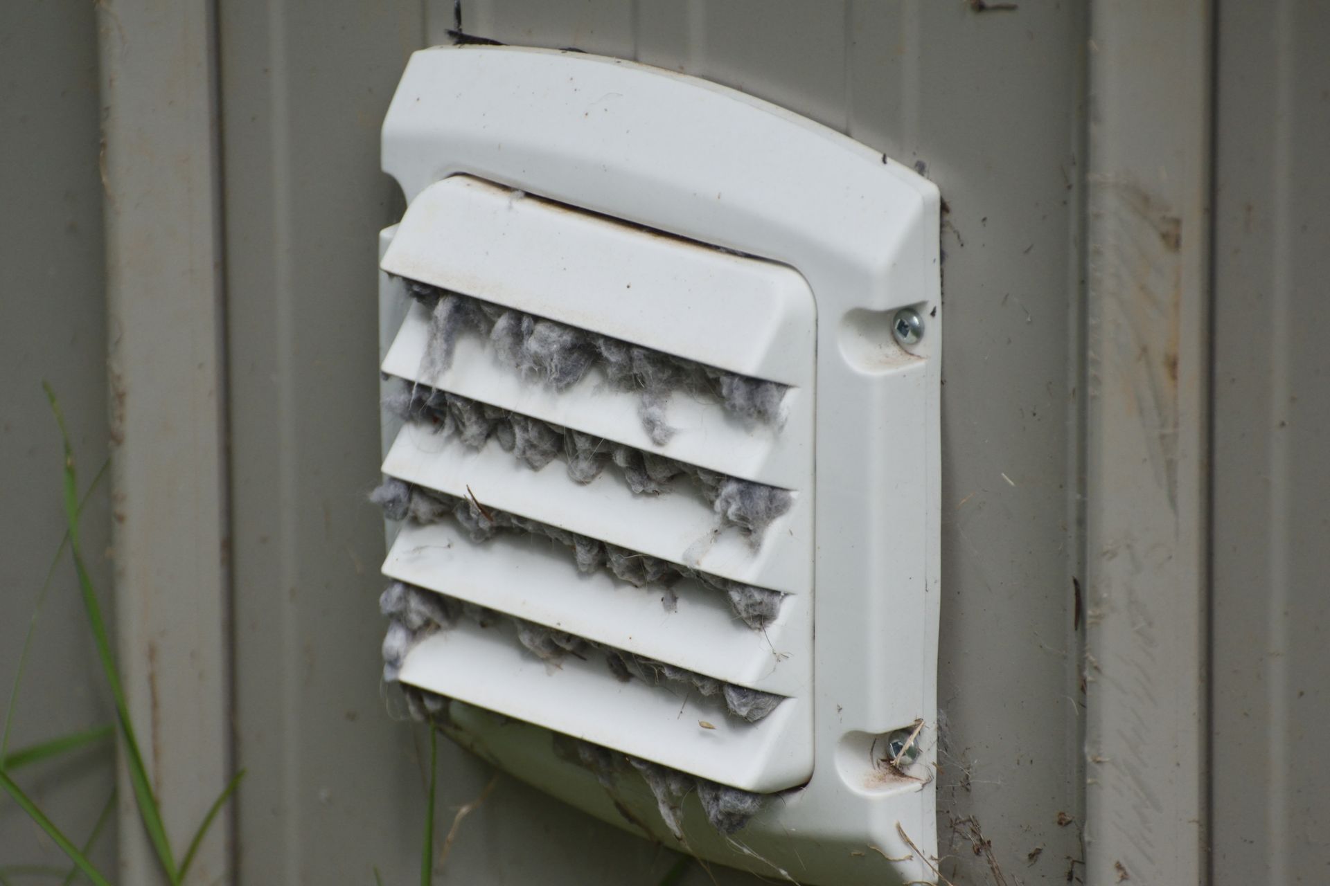 White exterior wall vent with horizontal slats and dust buildup mounted on a gray building wall