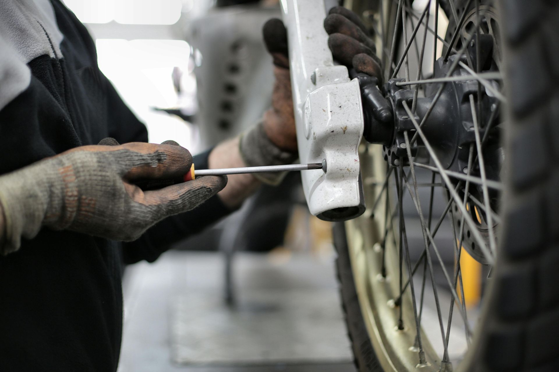 A person working on a motorcycle wheel with a screwdriver.