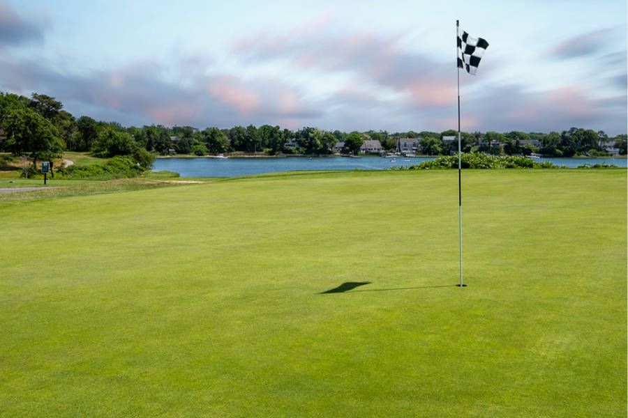 A golf course with a flag on the green and a lake in the background.