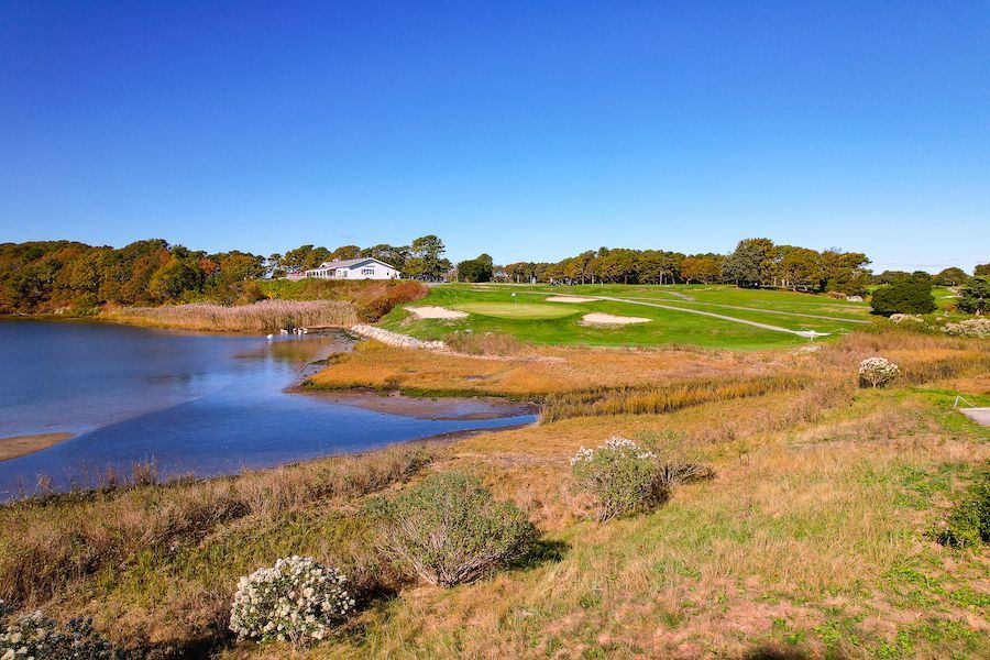 A golf course with a lake in the foreground and a house in the background.