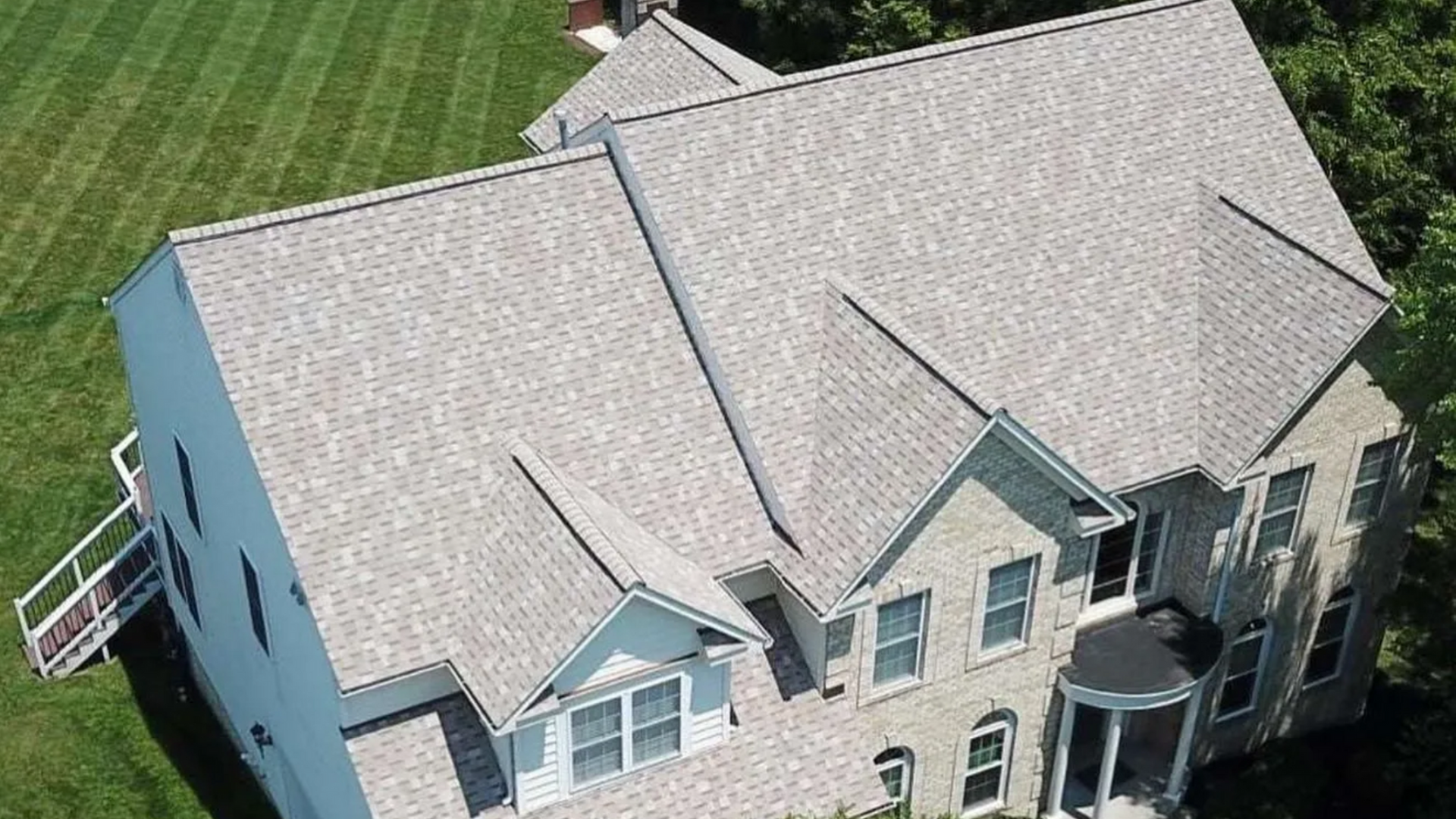 Two-story house with gray shingle roof, surrounded by green grass and trees.