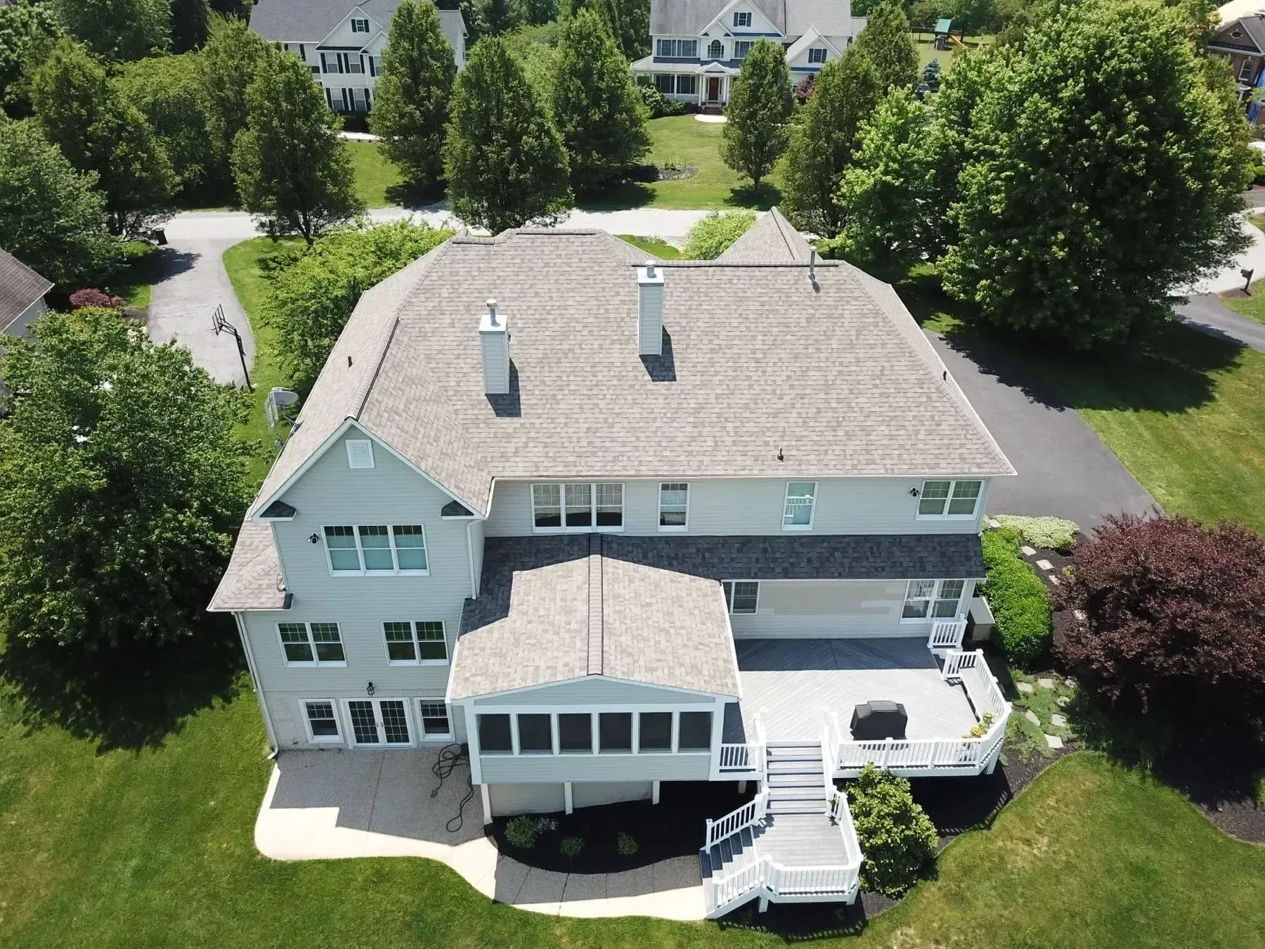 Aerial view of a two-story house with a deck and screened porch, surrounded by trees and grass.
