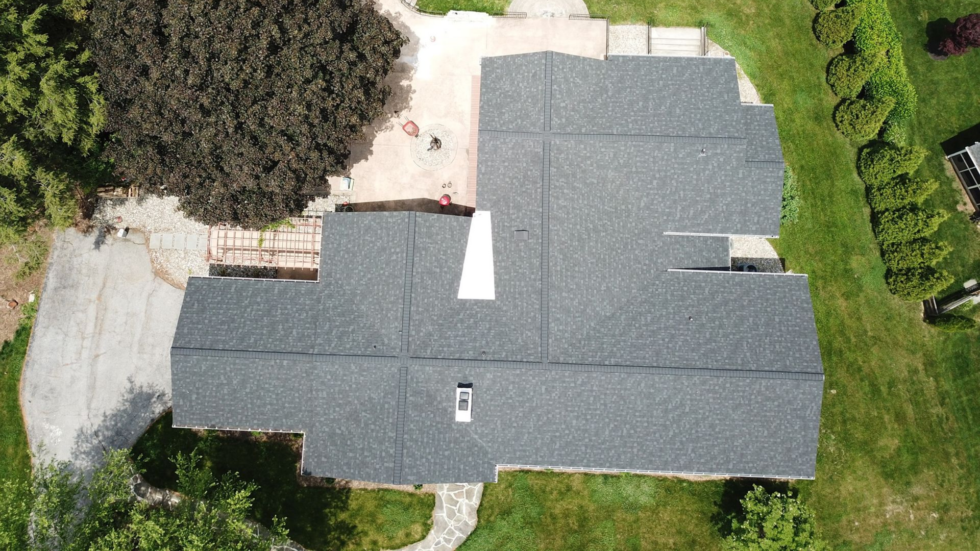 Overhead view of a dark gray shingled roof on a house with surrounding green grass and a tree.