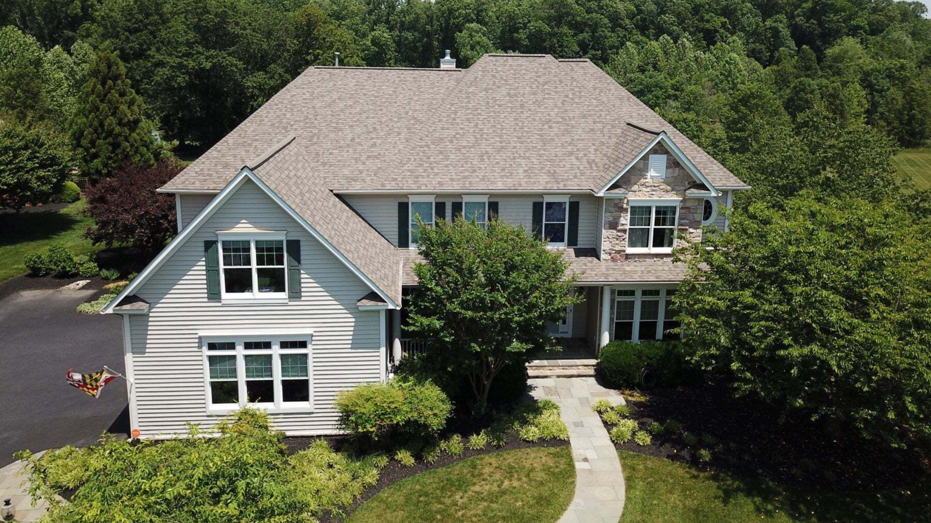 Two-story house with light siding and gray roof, surrounded by trees and landscaping.