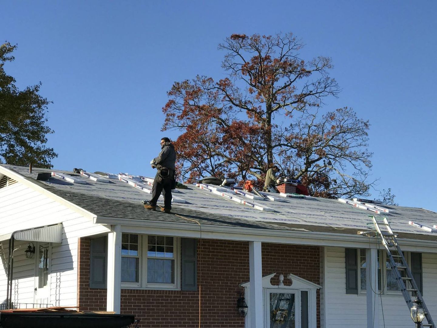 Roofing contractor laying new underlayment and shingles during a replacement project