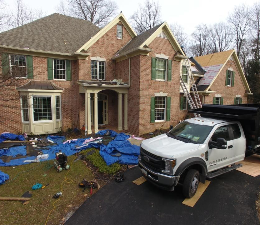 White pickup in front of a brick house with debris and blue tarp on the lawn after storm damage