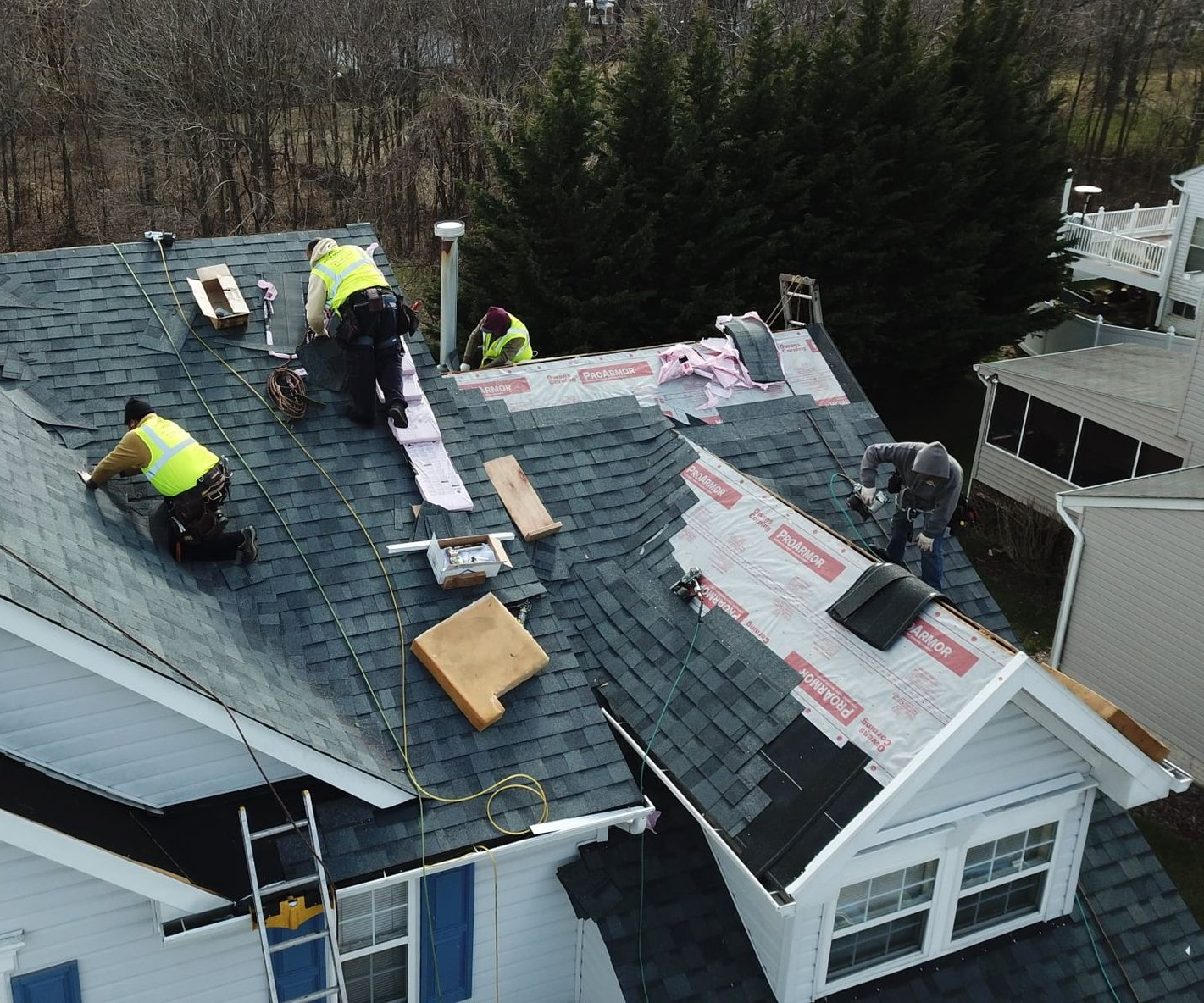 Roofers in yellow vests installing new shingles on a house roof.