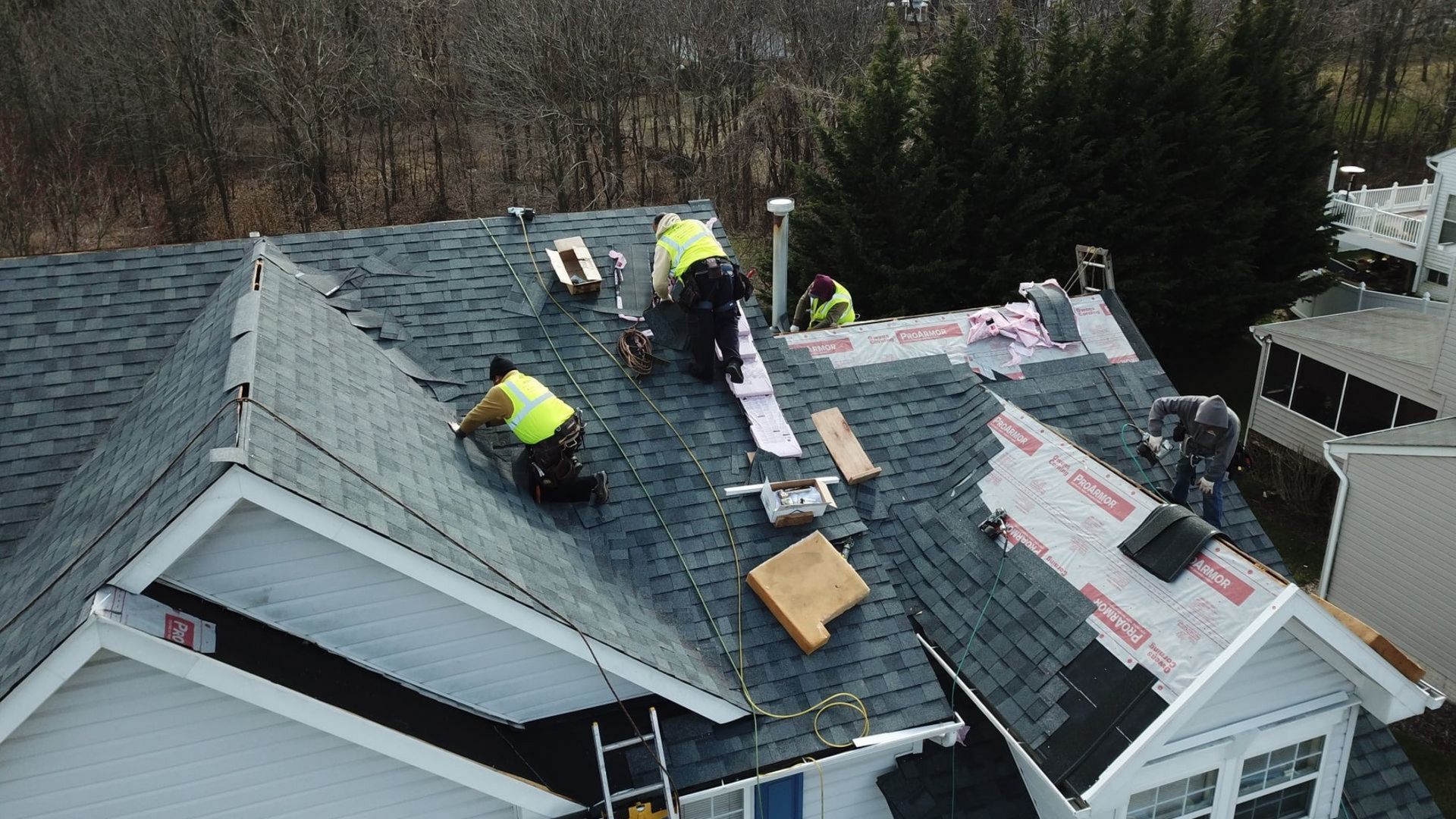 Roofers installing shingles on a house roof. Blue and gray shingles, workers wearing safety vests.