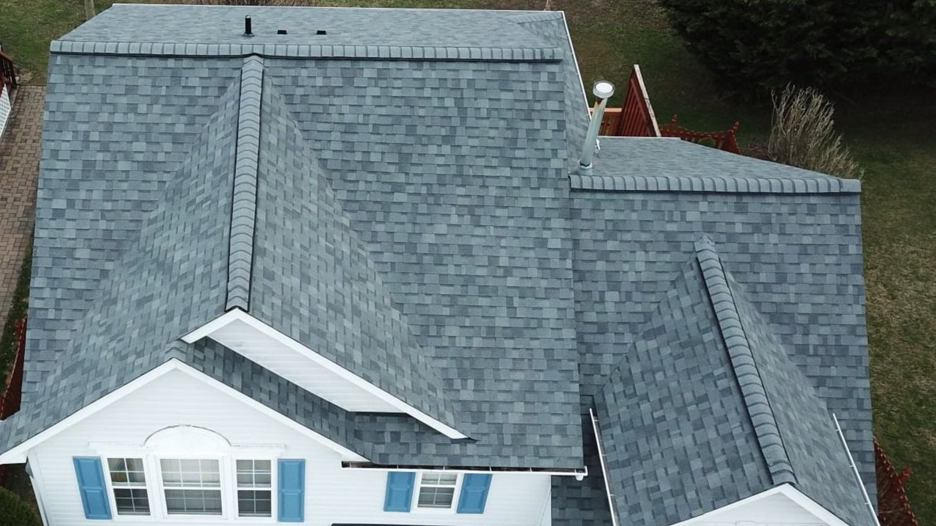 Overhead view of a house with a gray shingle roof and white siding; blue shutters on a window.