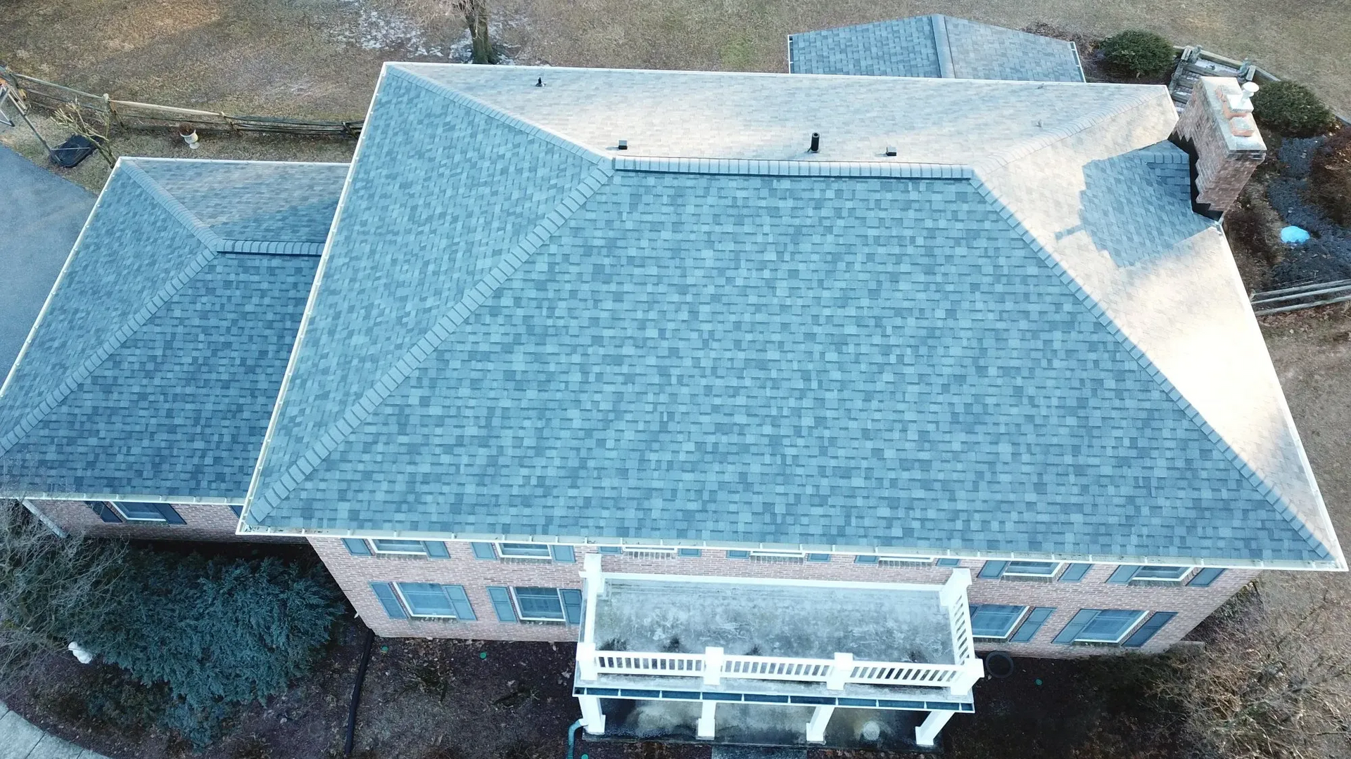 Overhead view of a brick house with a gray shingled roof and a white porch.