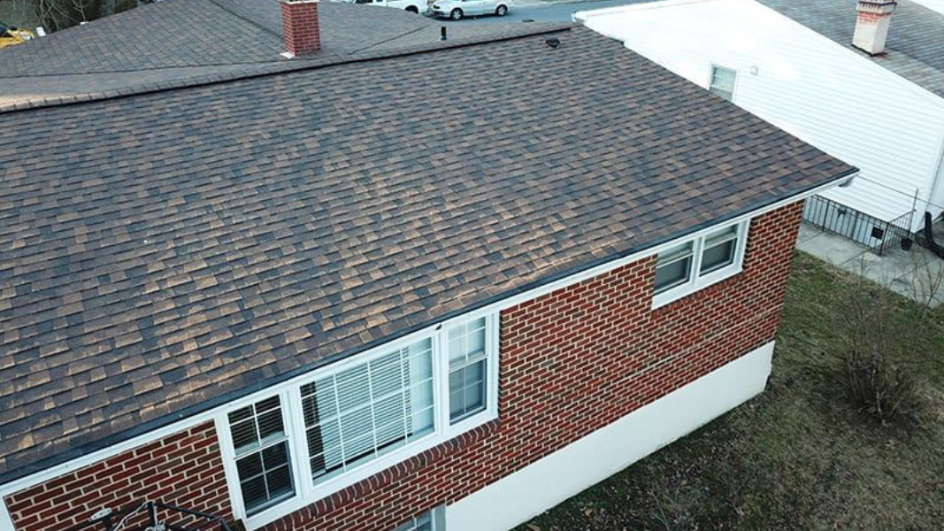 Brick house with brown roof, white trim windows, and a small patch of grass.