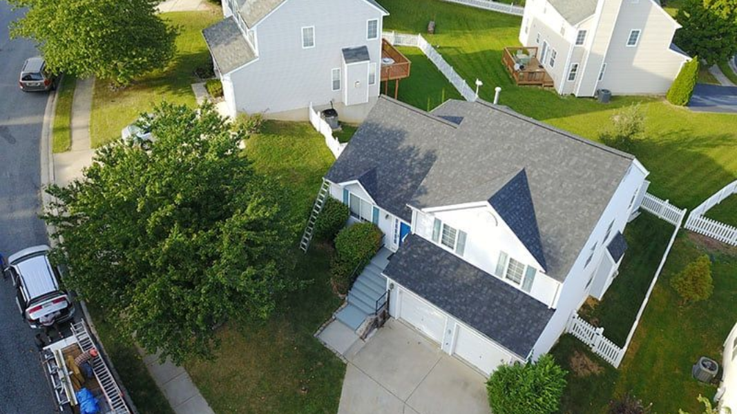 Aerial view of a white house with a gray roof and green lawn in a suburban neighborhood.