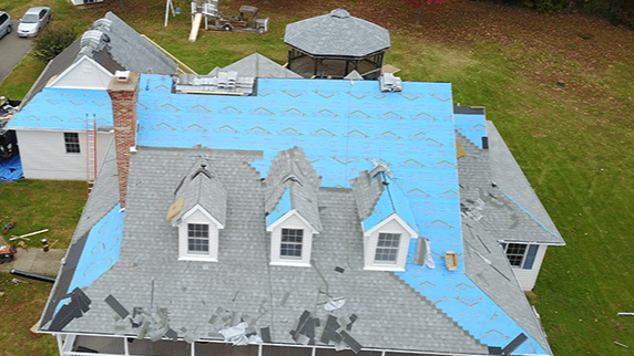 House roof partially covered with blue tarp during a repair, with three dormer windows.