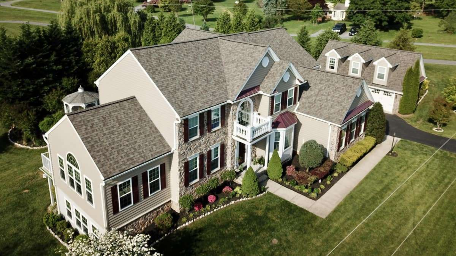 Aerial view of a two-story beige house with a grey roof and well-manicured lawn.
