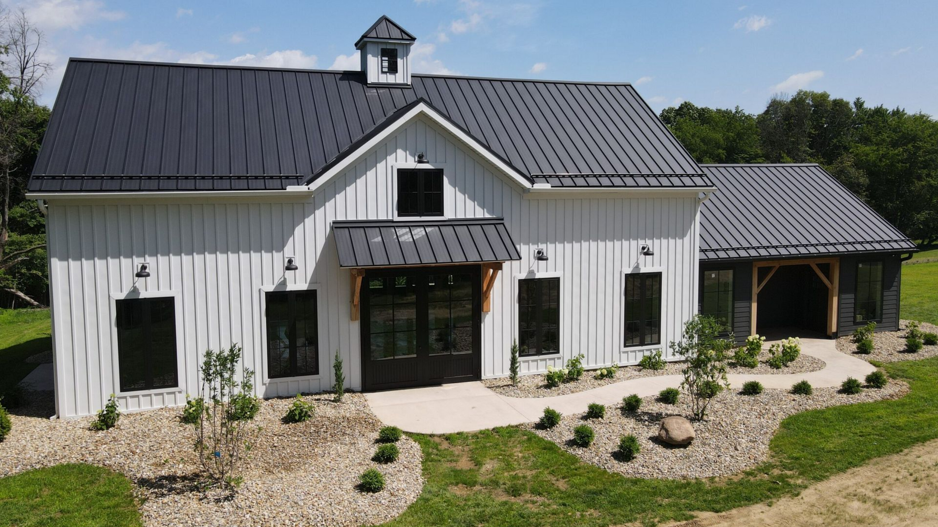 White barn-style building with black roof and trim. Exterior features landscaping and a clear, sunny sky.