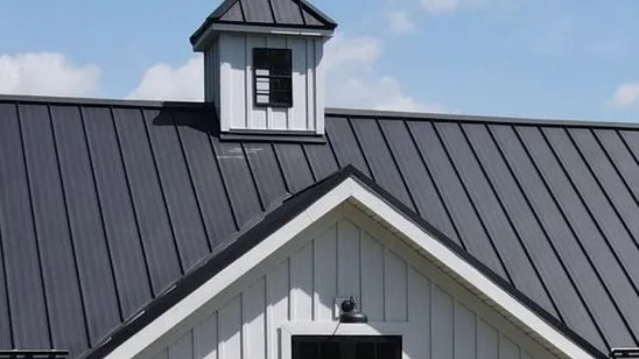 Dark metal roof with white trim and a small windowed cupola against a blue sky. Metal roof installation