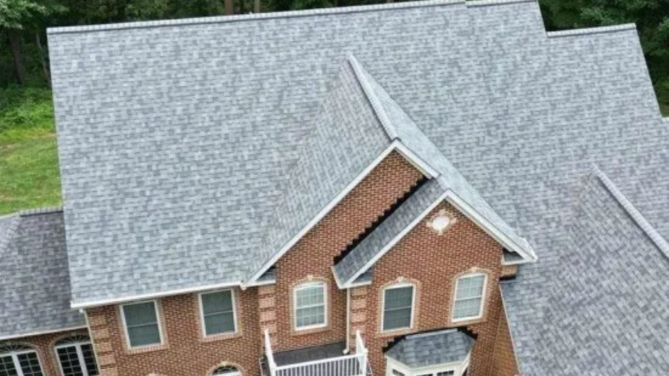 Aerial view of a house with gray shingle roof, red brick facade, and green surroundings.