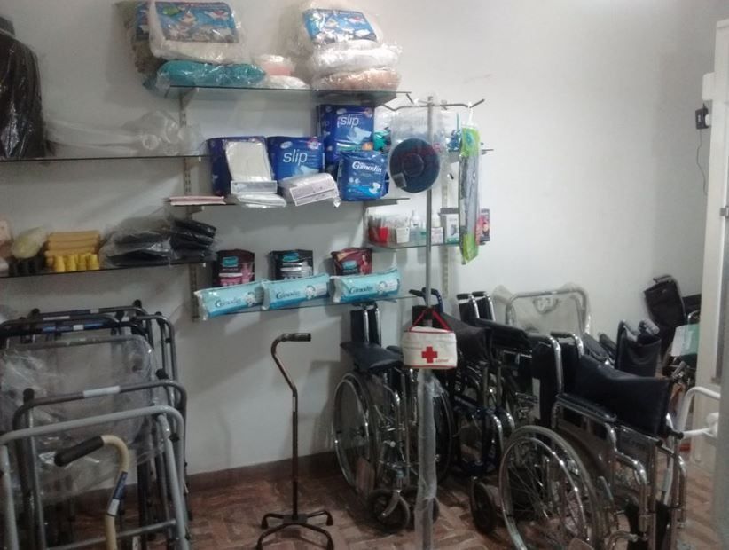 Estanterías repletas de suministros plegados junto a varias sillas de ruedas y andadores en un almacén.