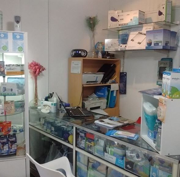 Recepción de una pequeña farmacia o clínica con estantes para medicamentos, un mostrador de cristal y cajas con suministros.