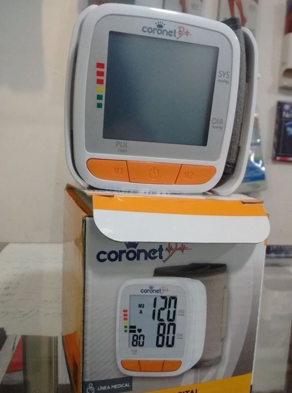 Dos tensiómetros digitales Coronet apilados en un estante, uno de ellos mostrando 120/80.