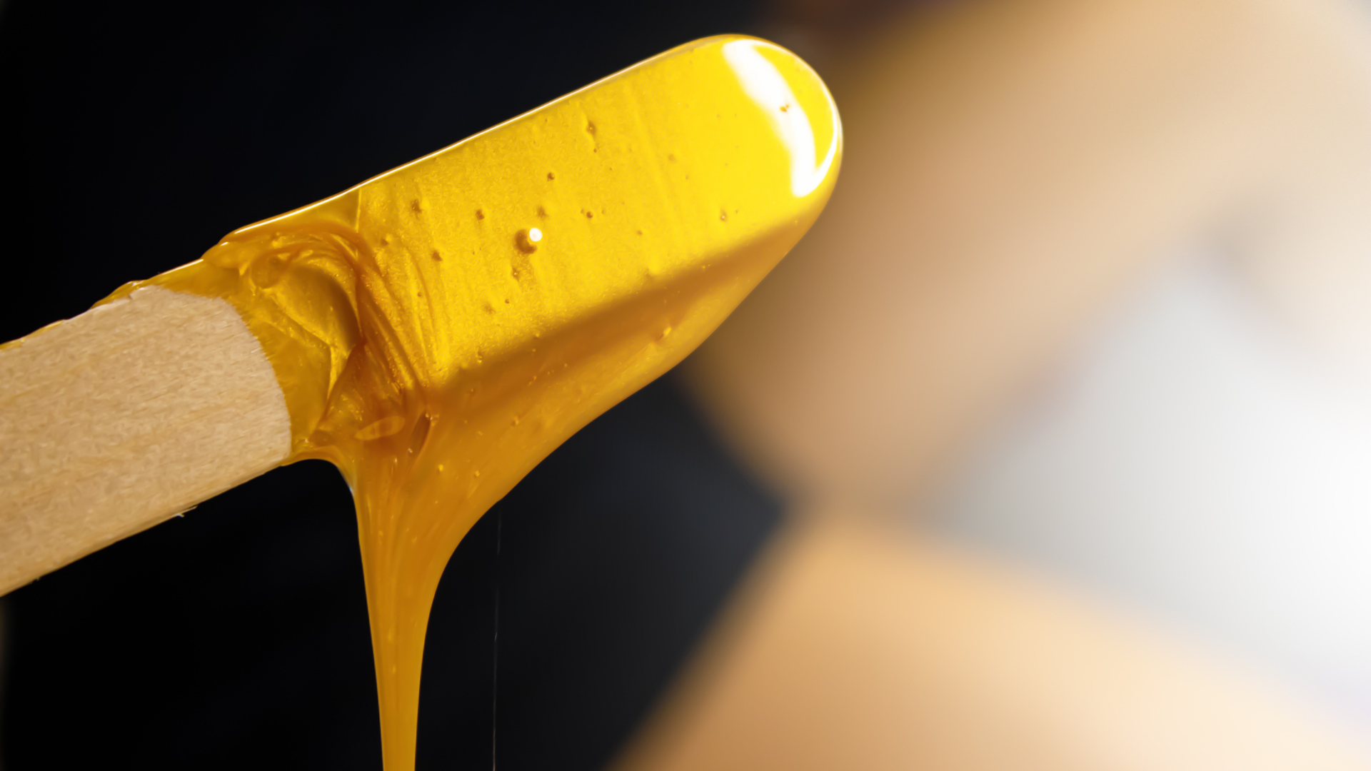 Wooden applicator with dripping yellow wax.