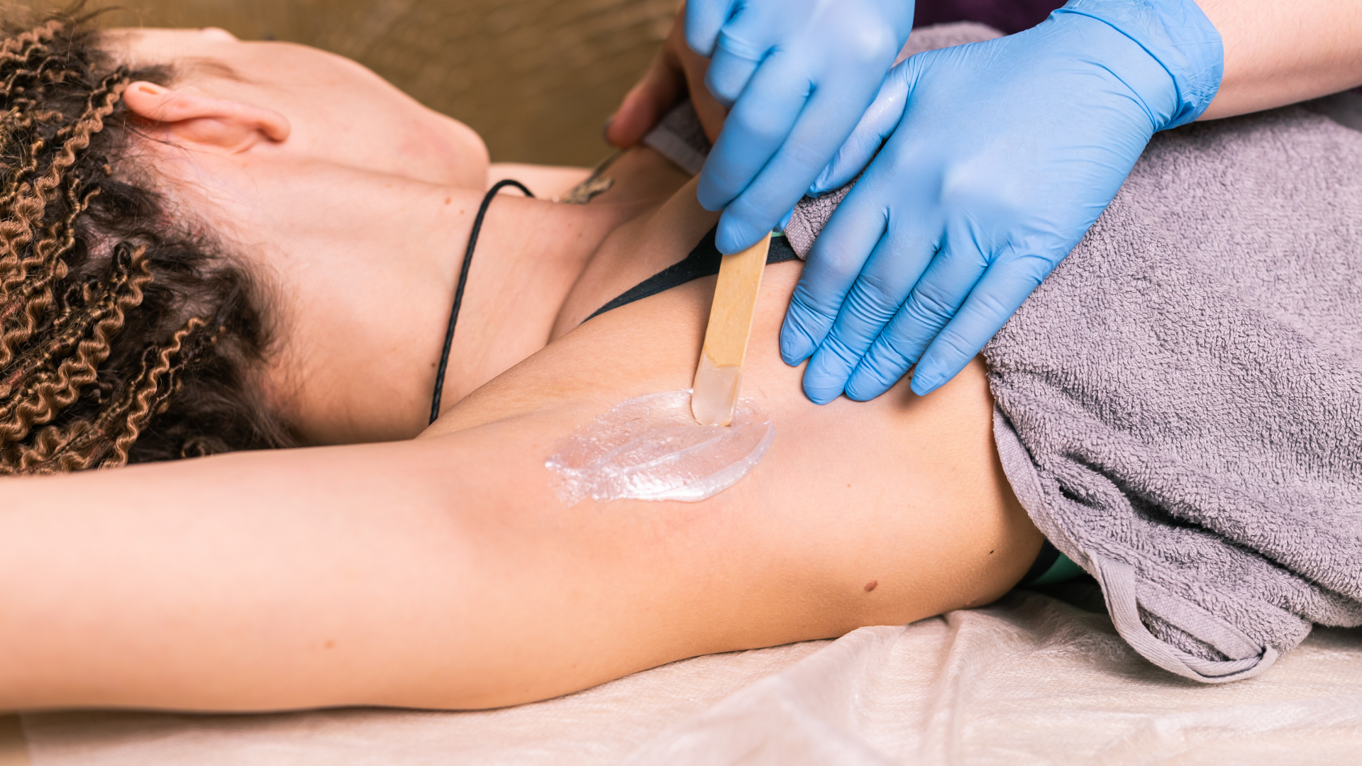 A person receiving an underarm wax treatment, hands wearing blue gloves.